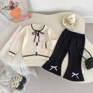 Detail of girl's knit cardigan with bow tie and flare pants with white ribbon accents