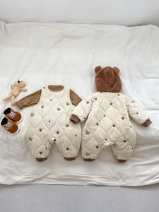 Detail of quilted baby rompers featuring bear patterns and 3D ears on white bedding