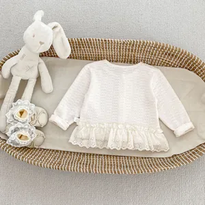 Dettaglio del cardigan neonato in maglia color crema con pizzo e bordo smerlato