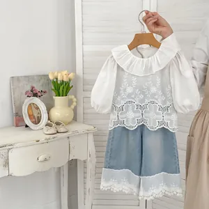 Detail of floral embroidery and lace trim on girl's white blouse and denim skirt set