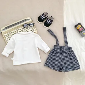 Detailed flat lay of boys' vintage plaid overalls and white bow tie shirt with baby shoes