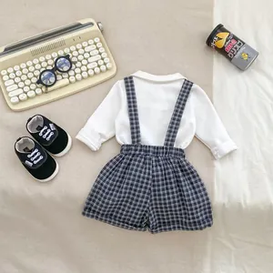 Detail view of baby boy plaid suspender shorts with white bow tie collared shirt