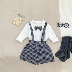 Detailed flat lay of toddler gentleman outfit with bow tie shirt and plaid suspender shorts