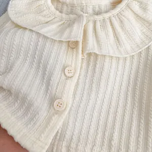 Detailansicht der cremefarbenen Babyjacke mit Rüschenkragen und vertikalem Strickmuster