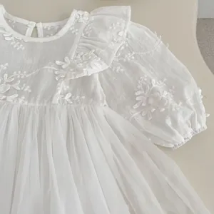 Detail of white infant dress featuring delicate floral embroidery and elegant ruffles