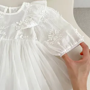 Detailed close-up of intricate white floral embroidery on baby princess dress fabric