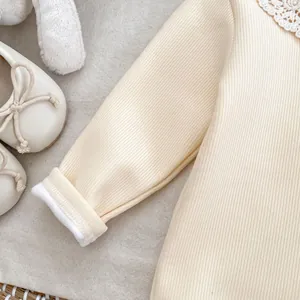 Détail d'un barboteuse bébé beige côtelé avec col en dentelle et poignets en peluche