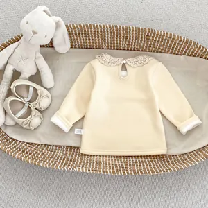 Détail d'un haut bébé en maille côtelée avec col en dentelle et bouton au dos jaune