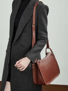 Minimalist brown pebbled leather crossbody bag with silver rivet details on grey coat
