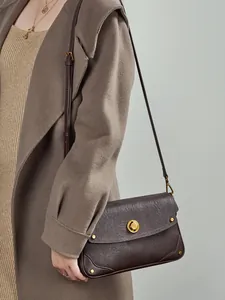 Sac bandoulière en cuir marron avec fermoir anneau doré porté par un mannequin