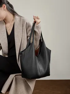Große schwarze Leder-Einkaufstasche mit Litschistruktur am Modell in minimalistischem Stil