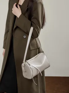 Sac Boston minimaliste en cuir gris clair porté sur un élégant manteau vert olive