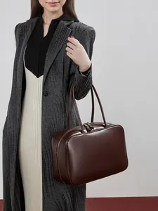Dark brown leather bowling bag for women shown with model in a minimalist setting