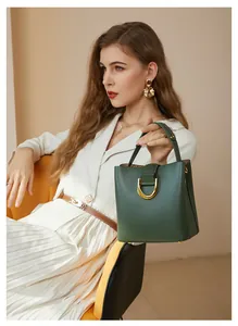Détail du sac seau en cuir vert foncé avec boucle dorée sur un mannequin en robe blanche