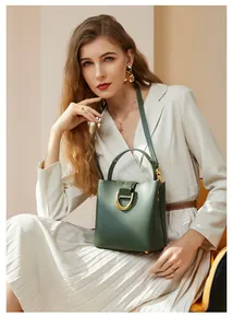Sac seau en cuir vert foncé avec fermoir fer à cheval doré porté par un mannequin chic