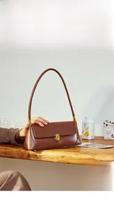 Detailed view of a brown leather baguette bag with a golden buckle on a wooden table