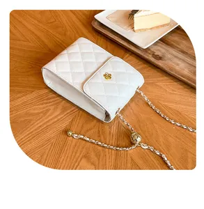 Details einer weißen gesteppten Umhängetasche mit goldener Blumenschnalle auf Holz