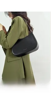Close-up of a minimalist black leather baguette bag worn by a model in an olive suit