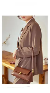 Close-up of brown leather baguette bag with gold buckle on female model in coffee suit