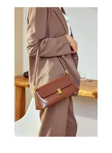 Detail view of brown leather baguette bag with elegant gold metal clasp and sleek profile