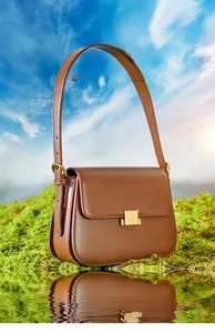 Detailed close-up of brown leather bag with gold buckle on moss against blue sky