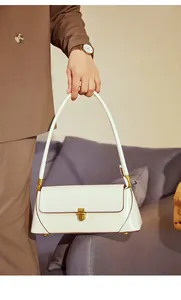 Detail of a minimalist cream baguette bag with vintage gold buckle and leather texture