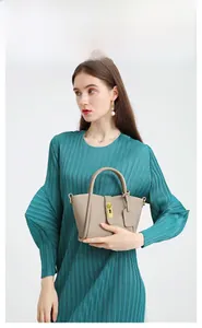 Detail of khaki leather bucket bag with gold hardware held by a model in a navy dress