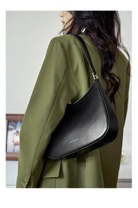Detail of black leather half-moon baguette bag with silver text and metal buckle