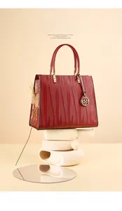 Red textured leather handbag displayed with dry wheat and artistic geometric props