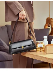 Detail of minimalist black leather baguette bag with a vintage gold lock and fine stitching