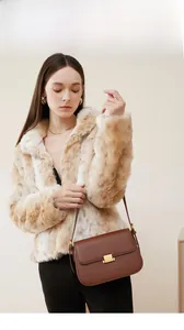 Close-up of brown leather bag with gold buckle on a model in a beige faux fur coat