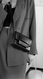 Detail of black woven matte leather shoulder bag with wide flap and decorative loop buckle