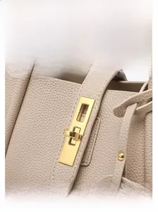 Close-up of golden metal twist lock and lychee grain leather texture on beige bucket bag