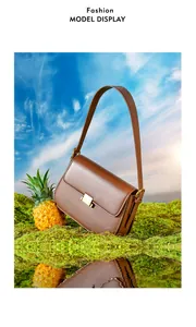 Detailed view of a brown leather shoulder bag with gold clasp set against a creative nature scene