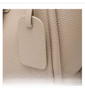 Detail of beige lychee grain leather bucket bag featuring a detachable rectangular charm
