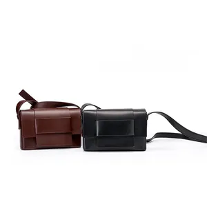 Detail of minimalist leather crossbody bags in black and dark brown with wide buckled straps
