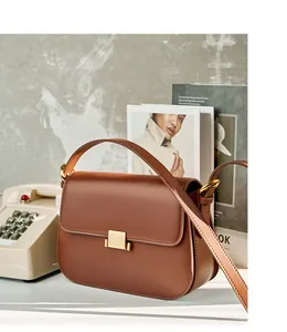Detail view of brown leather handbag with gold square buckle in a retro aesthetic scene