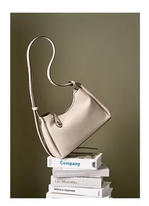 Détail d'un sac à bandoulière en cuir grainé crème posé sur des livres élégants