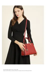 Detail of red leather handbag with wave embossing and gold logo charm on black dress