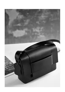 Close-up of minimalist black matte leather crossbody bag featuring wide strap and charm
