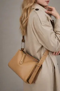 Borsa a cuscino minimalista in pelle kaki indossata a tracolla su un trench alla moda