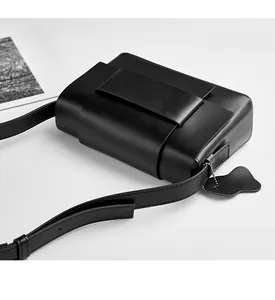 Close-up of black leather crossbody bag with wide strap and heart charm on white background