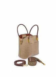 Dettaglio della borsa a secchiello in pelle beige con manici marroni e due tracolle