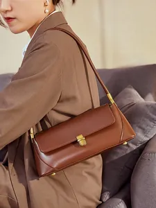 Brown leather baguette shoulder bag with gold metal buckle shown on model in a home setting