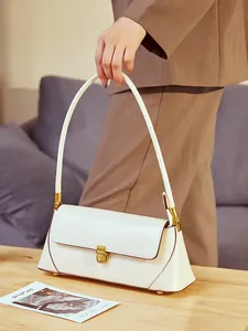 Minimalist white leather baguette bag with vintage gold buckle on wooden table