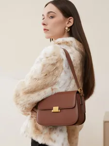Brown leather crossbody bag with rectangular gold buckle worn with faux fur coat