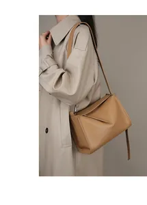 Dettaglio borsa a spalla in pelle kaki con design geometrico indossata su cappotto beige