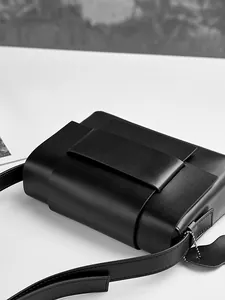 Minimalist black leather crossbody bag with wide strap detail and hanging tag charm