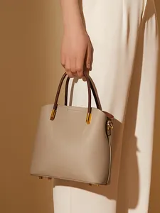 Borsa a secchiello minimalista in pelle beige con manici marroni e dettagli in metallo dorato