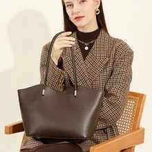 Dunkelbraune matte Leder-Tote-Bag mit Silberakzenten, getragen von Model im Karo-Blazer